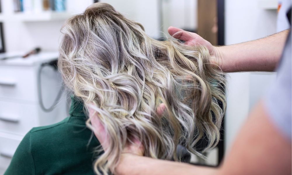 Stylist using hooded salon hair dryer on curly hair