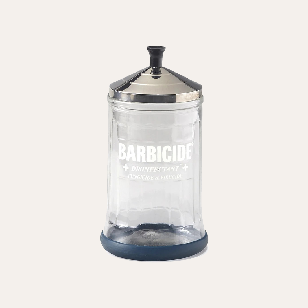 A clear plastic canister of barbicide disinfectant with a silver metal lid, a dark blue base, and white printed text on the front, 