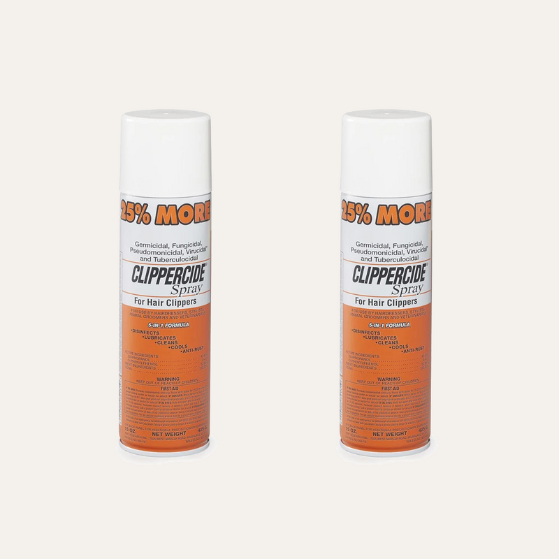 Two aerosol cans of ClipperCide Spray for hair clippers, shown side by side on a plain light beige background. The cans are white with orange and black labeling.