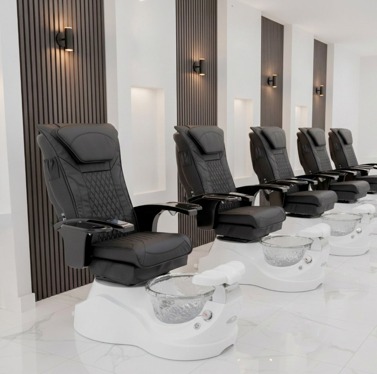 Row of black pedicure chairs in a spa setting with white bowls.