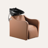 A tan quilted salon shampoo chair with a black ceramic wash bowl mounted on the back, shown against a solid off-white background.